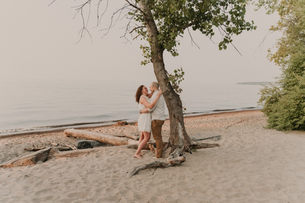 Stephen and Malayna leaning on a tree on a beach in Rochester